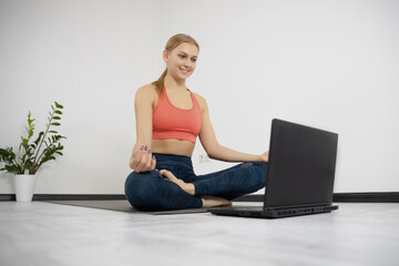 Athletic young female in comfortable stylish sportswear watching yoga class online on laptop on fitness carpet