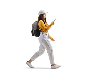 Full length profile shot of a female student walking and typin on a mobile phone