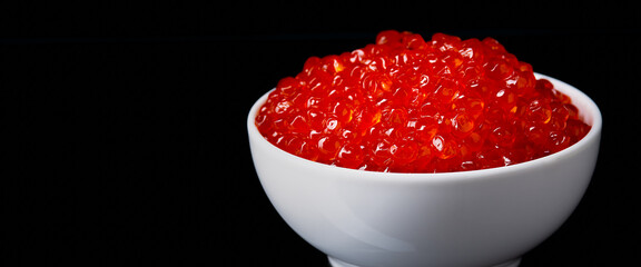 Red caviar in a white cup on a black background with a reflection.