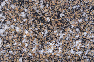 close up of frozen asphalt in winter where you can see colored stones