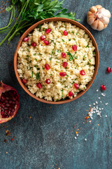 Cooked couscous with parsley and pomegranate in a ceramic bowl on a dark background top view. Maghreb cuisine, vegan food. Copy space for text