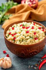 Cooked couscous with parsley and pomegranate in a ceramic bowl on a dark background close-up. Maghreb cuisine, vegan food.