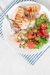 Grilled turkey steaks and lettuce salad with grapefruit in a plate on a white concrete table top view. Healthy diet food. Tasty lunch with turkey meat.