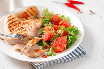 Grilled turkey steaks and lettuce salad with grapefruit in a plate on a white concrete table close-up. Healthy diet food. Tasty lunch with turkey meat.
