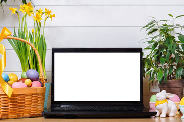 A laptop with a blank screen on a table festively decorated for the Easter holiday