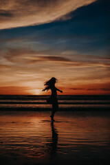 Woman enjoying sunset at the beach. Golden hour sunset. Sunset seascape. Bright sunlight. Ocean with waves. Island Bali, Indonesia