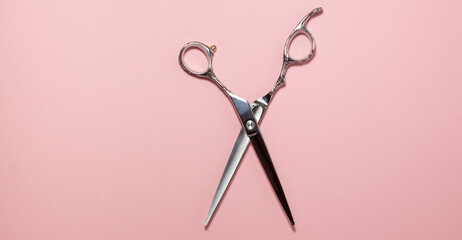 Flat lay of professional hair cutting shears in the centre of the frame on bright pink background. Hairdresser salon equipment concept with copy space