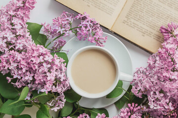 spring composition flat lay white cup of coffee, pink lilac beautiful bouquet of lilacs, old book, concept of spring and comfort 