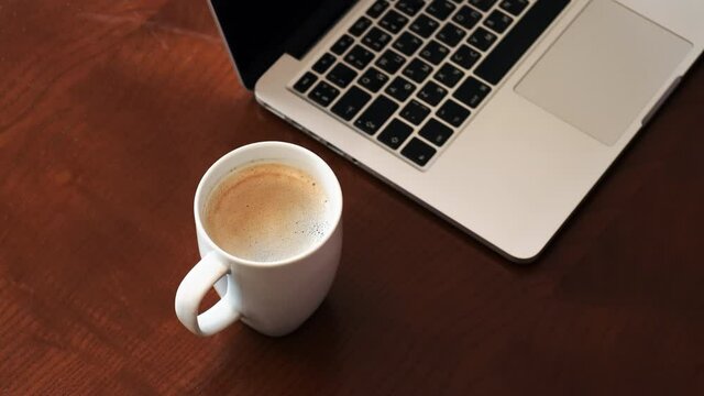 A man puts a cup of coffee, laptop on the wooden table. Top view