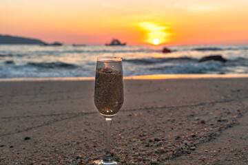 A glass of water was put with sand on the beach of Patong Phuket at sunset..