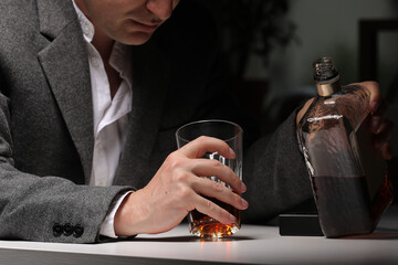 man pours alcohol into a glass in the kitchen after work. Young man suffering from severe headache or migraine sitting with a glass of whiskey in the kitchen. alcohol dependence