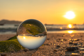 Fototapeta na wymiar A crystal ball rests on the sandy pebbles of Kalim Beach. In the crystal ball, you will see an upside down view of the sunset..