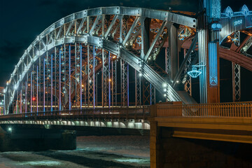 the beautiful metal bridge of Peter the Great across the Neva River in St. Petersburg against the night sky