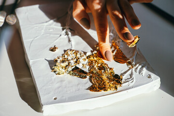 Close-up female hands working with plaster relief and golden foil. DIY and art hobby concept.
