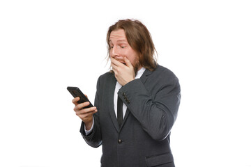 Portrait of surprised businessman with a beard and long hair in formal suit looks at mobile phone isolated on white background.