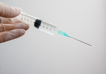 Medical syringe loaded and ready to inject held by a gloved hand on a white background.