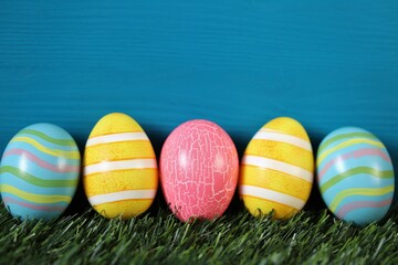 Easter holiday.Multicolored striped easter eggs set on green grass on turquoise background..Spring festive easter background. copy space. Easter egg hunt
