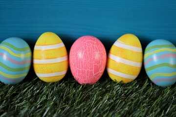 Easter holiday.Multicolored striped easter eggs  on green grass on bright turquoise background..Spring festive easter background. copy space. Easter egg hunt