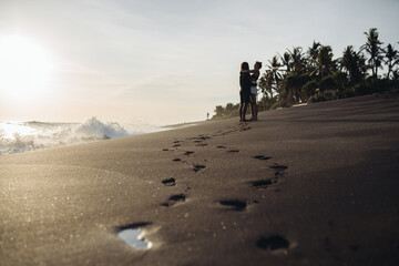 on the black coastal sand in the distance amid palm trees hugged by a loving couple. High quality photo