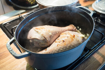 marinated and spiced turkey leg with various vegetables in the casserolle, cooking on the stove.