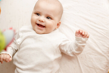 Adorable baby in sunny bedroom. Newborn baby is resting in bed. Smiling child looking at toys.