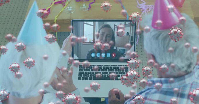 Animation of covid 19 cells floating over senior couple in party hats using laptop on video call