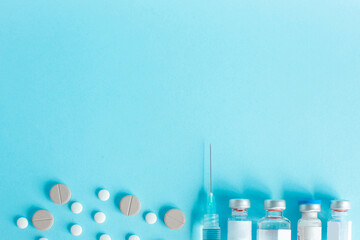 Syringe and vial drug with round tablet as a border on a blue background with copy space