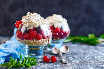 Recipe ideas for summer diet breakfast, healthy morning dessert in portioned jars with summer berries - raspberry, cherries, blackberry. On stone background.