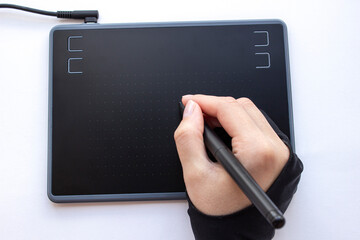 A person draws on a graphics tablet. A hand in a drawing glove holds a touch pen. A wireless...