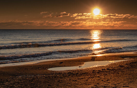 sunrise at the beach. waves crashing on the shoreline while the sun rises at dawn. golden hour in the morning. reflection of the sunrise on the lake.