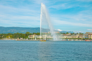 View of Jet d'eau fountain or water jet fountain, harbor and Geneva Lake. The most famous attraction and symbol of Geneva. Swiss Alps and skyline cityscape, on background. French Swiss Switzerland