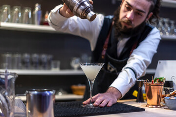 Bartender pouring fresh alcoholic drink into the glasses with ice cubes on the bar counter