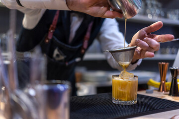 Bartender pouring fresh alcoholic drink into the glasses with ice cubes on the bar counter