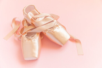 New pastel beige ballet shoes with satin ribbon isolated on pink background. Ballerina classical pointe shoes for dance training. Ballet school concept. Top view flat lay, copy space