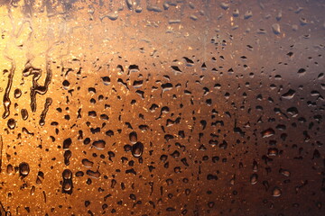 Window transparent glass with condensation, high humidity in the room, large drops of water flow down, warm tone, natural drops