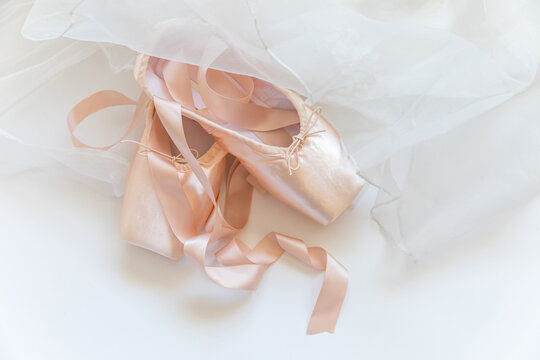 New pastel beige ballet shoes with satin ribbon and tutut skirt isolated on white background. Ballerina classical pointe shoes for dance training. Ballet school concept. Top view flat lay, copy space