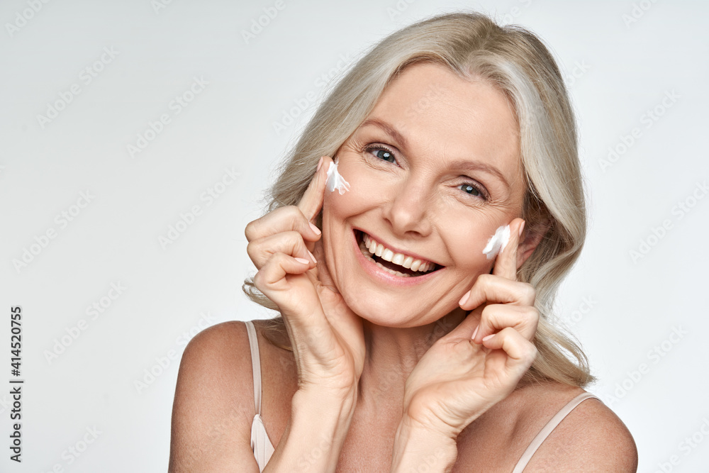 Sticker happy 50s mid aged mature old blonde lady applying facial cream on face skin laughing enjoying anti 