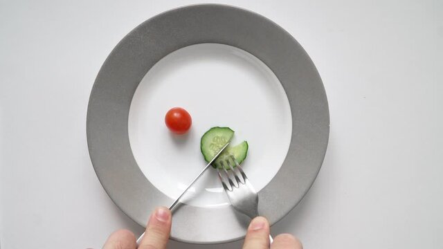 Man on diet eats little chili tomato and cucumber from plate. Concept of slimming and healthy food. Natural ingredients. Vegetables and healthy eating. Portion control. No animal byproducts. Top view