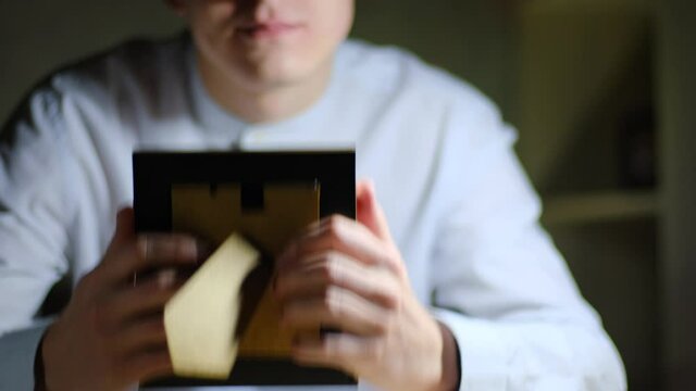 Nostalgia, memories concept. Young guy holding a framed photo in his hands and clutching it to his chest