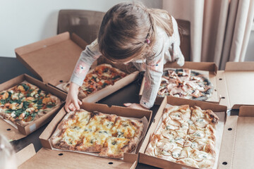 Lots of boxes with pizza pieces. Little girl eating at table. Cheese, pear, sausage, shrimp filling. Family lunch, birthday home party.Isolation food delivery, online order.Kids favorite harmful food