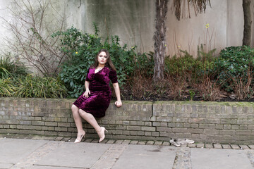 Portuguese woman with long straight hair and purple dress posing next to a garden