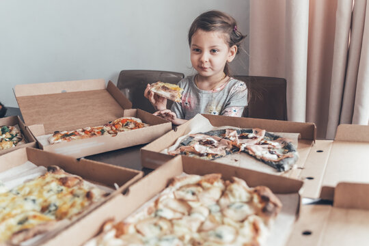 Lots of boxes with pizza pieces. Little girl eating at table. Cheese, pear, sausage, shrimp filling. Family lunch, birthday home party.Isolation food delivery, online order.Kids favorite harmful food