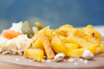 Roasted potatoes seasoned with salt, herbs and paprika on wooden board. Roast potato with pickles and sauerkraut.