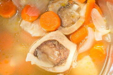 vegetable beef soup with marrowbone, carrots, onions, celery and globules of grease floating on soup