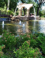 Fototapeta na wymiar Park with a pond, fountain, trees and flowers on a summer sunny day