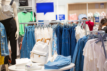 Women's jeans wear on hangers and shelves in a clothing store. Set denim casual wear for ladies. Fashionable and style. Boutique in the mall. Blurred background with copy space. Discounts and sale.