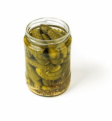 Delicious pickled cornichons in an open glass jar isolated on white background. Whole green gherkins marinated with dill and mustard seeds. Crunchy baby pickles. Tasty canned vegetables.