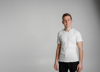 
teen guy looking into the frame surprised can't believe raised eyebrows
 and sincerely smiling with white teeth on the right side of the frame on a white background in a white T-shirt