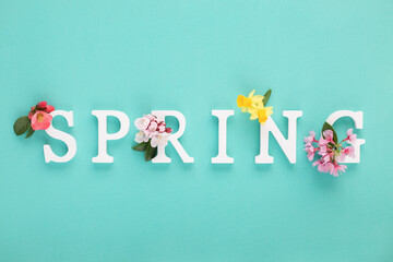White wooden letters make up a spring arrangement of fresh spring flowers on blue tiffany background. Minimal concept. Flat lay.