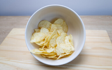 Potato chips with parsley and onion on a cutting board in a bowl on a table with different textures and colors in yellow and orange. Snack widely used in meetings of friends.